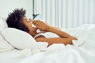 Buy stock photo Cropped shot of an attractive young woman blowing her nose and lying in bed at home