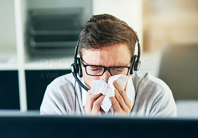 Buy stock photo Shot of a young call centre agent blowing his nose while working in an office