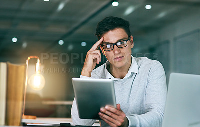 Buy stock photo Shot of a handsome young businessman using a digital tablet in an office at night