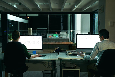 Buy stock photo Rearview shot of two businesspeople working on computers in an office at night