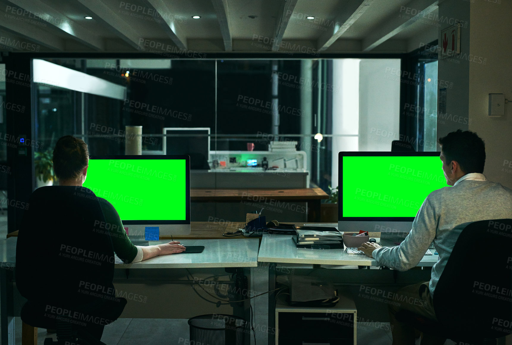 Buy stock photo Rearview shot of two businesspeople working on computers in an office at night