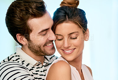 Buy stock photo Shot of a cheerful young couple holding each other while looking at the camera and standing inside at home during the day