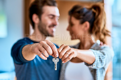 Buy stock photo Shot of a cheerful young couple holding a key together to their new home while standing inside during the day