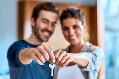 Buy stock photo Portrait of a cheerful young couple holding a key together to their new home while standing inside during the day