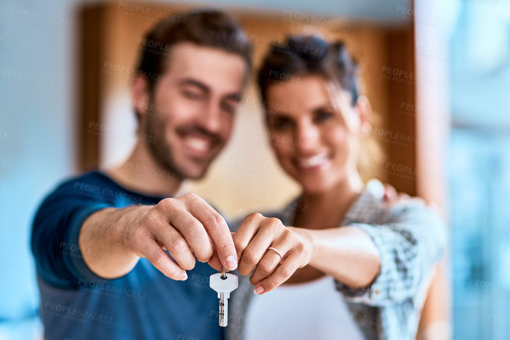 Buy stock photo Portrait of a cheerful young couple holding a key together to their new home while standing inside during the day