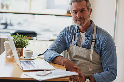 Buy stock photo Portrait of a handsome mature man doing some paperwork and using a laptop in his cafe