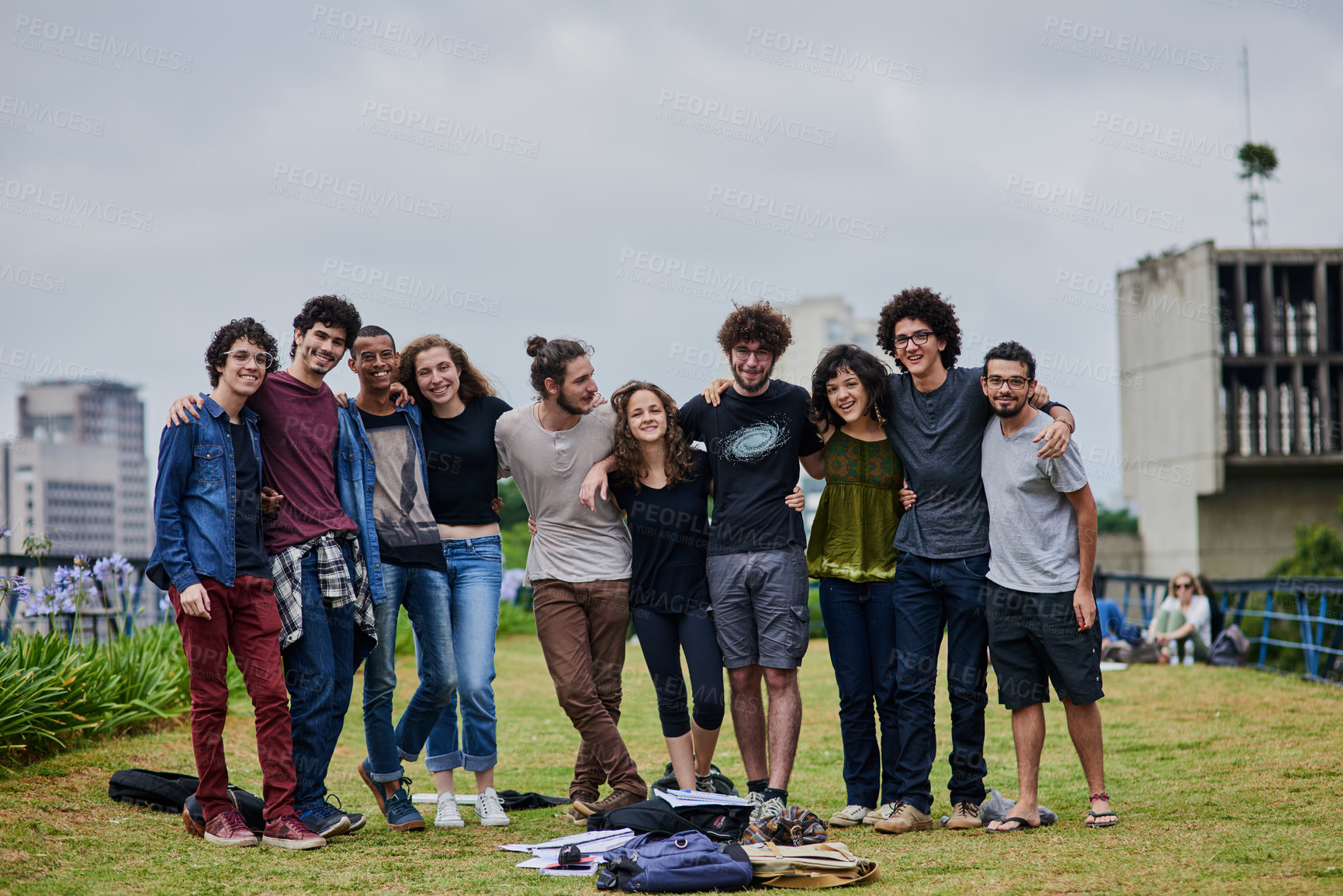 Buy stock photo Portrait of a group of young students standing arms around each other outside in a park during the day