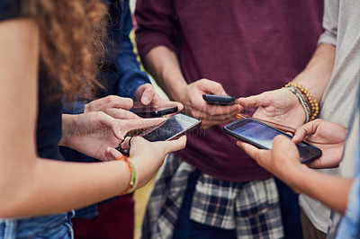 Buy stock photo Shot of a group of young unrecognizable people standing in a circle while browsing on their mobile phones outside during the day