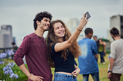 Buy stock photo Shot of two cheerful young friends taking a self portrait together with a mobile phone outside during the day
