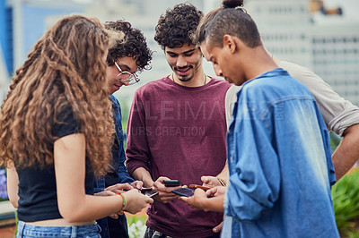Buy stock photo Shot of a group of young students standing in a circle while browsing on their mobile phones outside during the day
