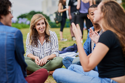 Buy stock photo Shot of a group of young students studying together while being seated in a park outside during the day
