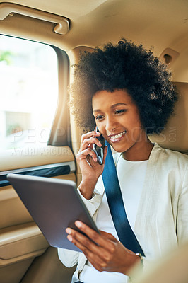 Buy stock photo Shot of a cheerful young businesswoman browsing on her digital tablet and making a phone call while being seated in a car on her way to work