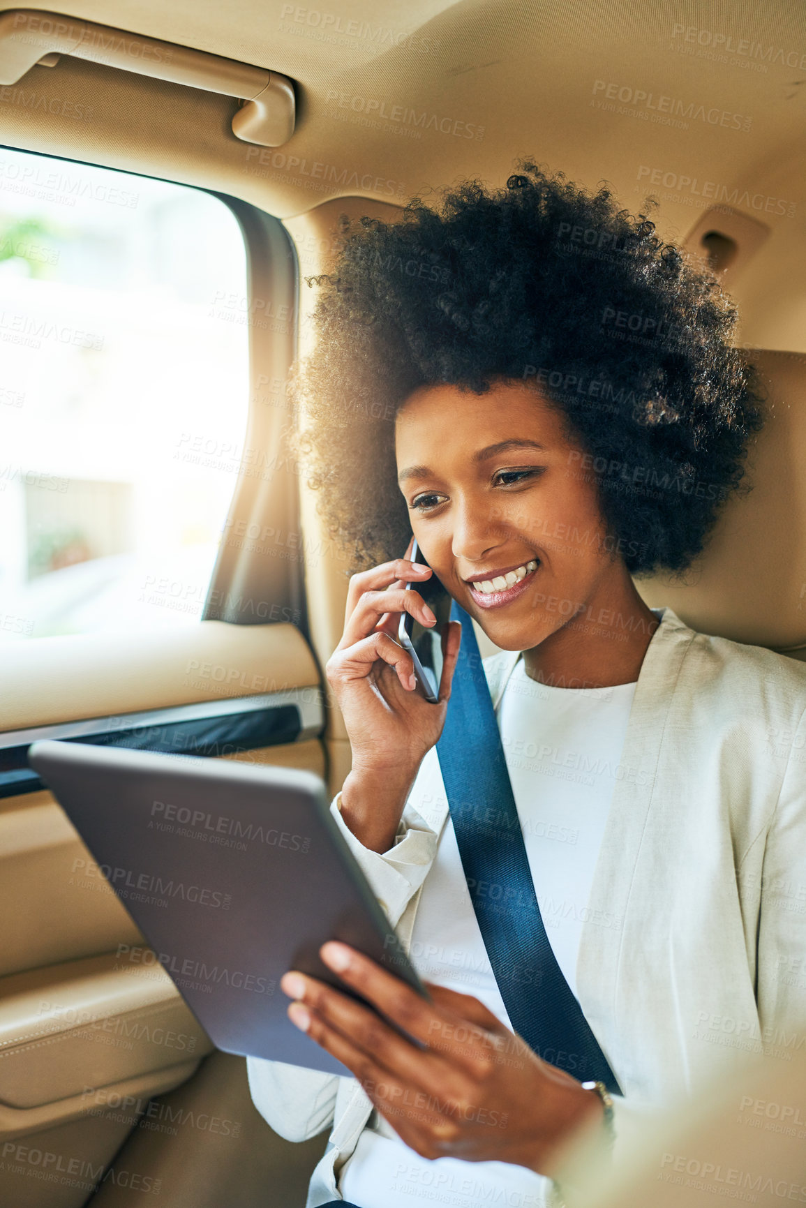 Buy stock photo Shot of a cheerful young businesswoman browsing on her digital tablet and making a phone call while being seated in a car on her way to work