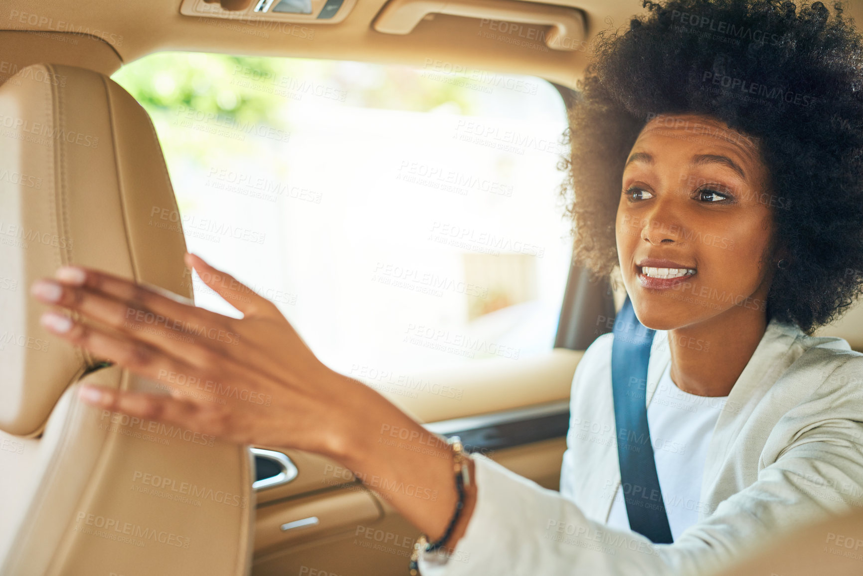 Buy stock photo Shot of a cheerful young businesswoman seated in a passenger seat of a car while giving direction to her work during the day