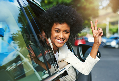 Buy stock photo Portrait of a cheerful young businesswoman driving in a car to work while leaning out of the vehicle and showing the peace sign