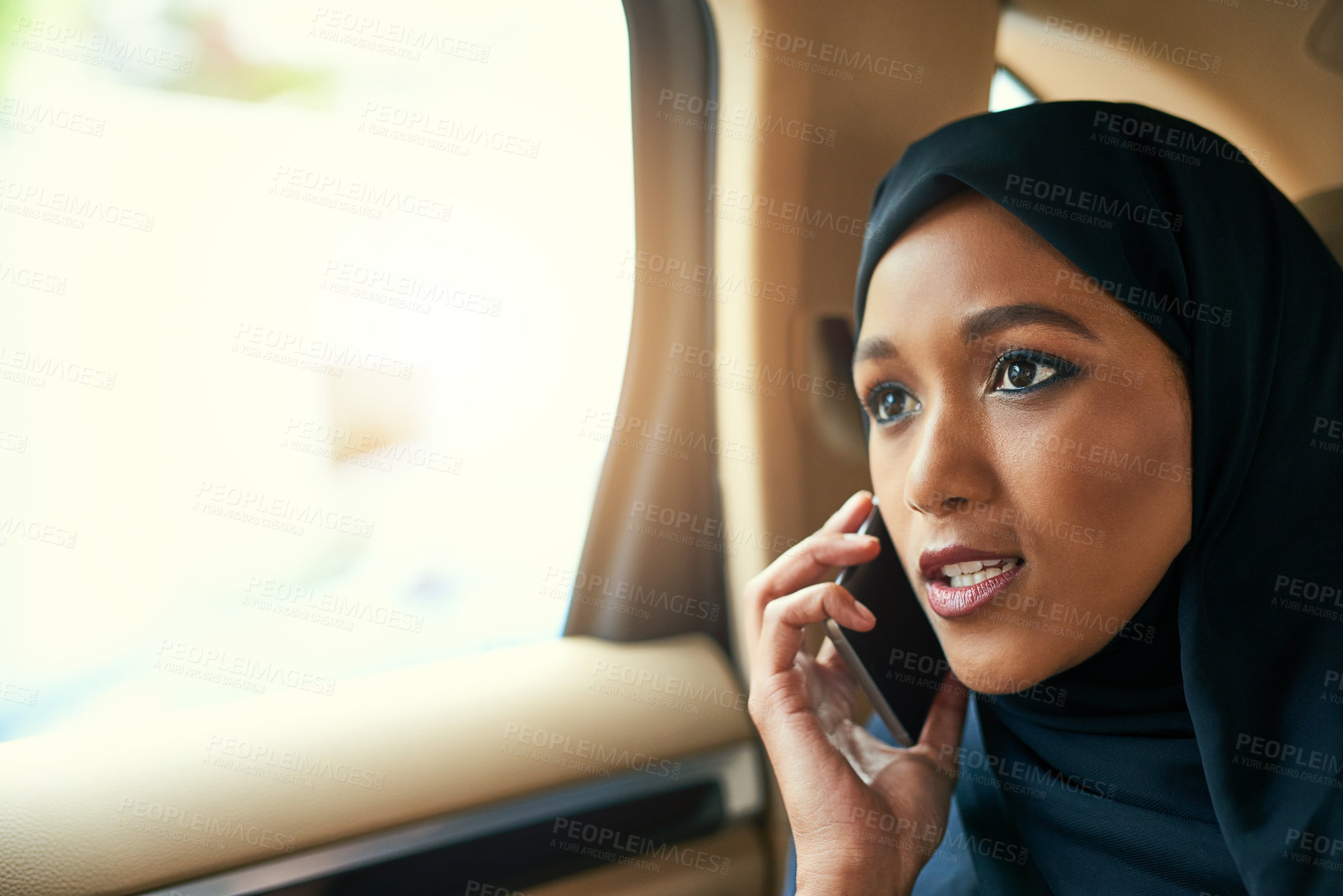 Buy stock photo Shot of a focused young businesswoman talking on her mobile phone while being seated in the back of a car on her way to work