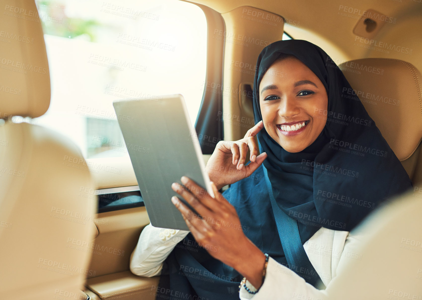 Buy stock photo Portrait of a cheerful young businesswoman browsing on a digital tablet while seated in the backseat of a car driving to work during the day