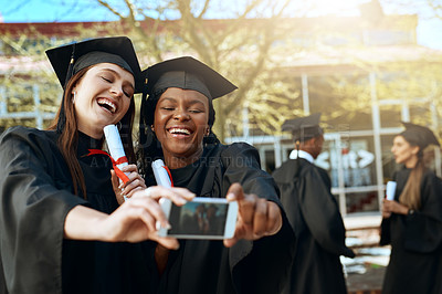Buy stock photo Shot of two young women taking selfies with a mobile phone on graduation day