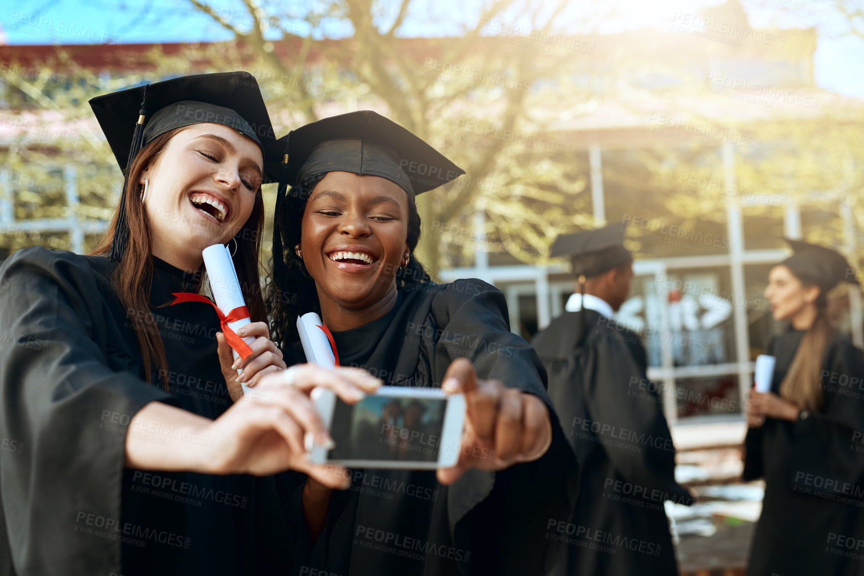 Buy stock photo Shot of two young women taking selfies with a mobile phone on graduation day