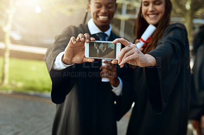 Buy stock photo Shot of a young man and woman taking selfies with a mobile phone on graduation day