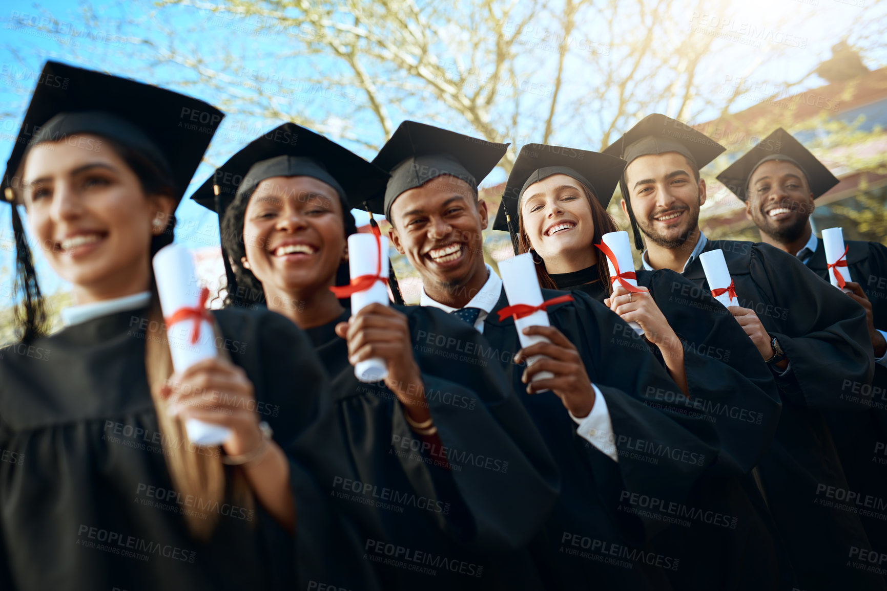 Buy stock photo Portrait of a group of young students holding their diplomas on graduation day