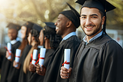 Buy stock photo Portrait of a young man holding his diploma while standing with his fellow students on graduation day