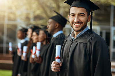 Buy stock photo Portrait of a young man holding his diploma while standing with his fellow students on graduation day
