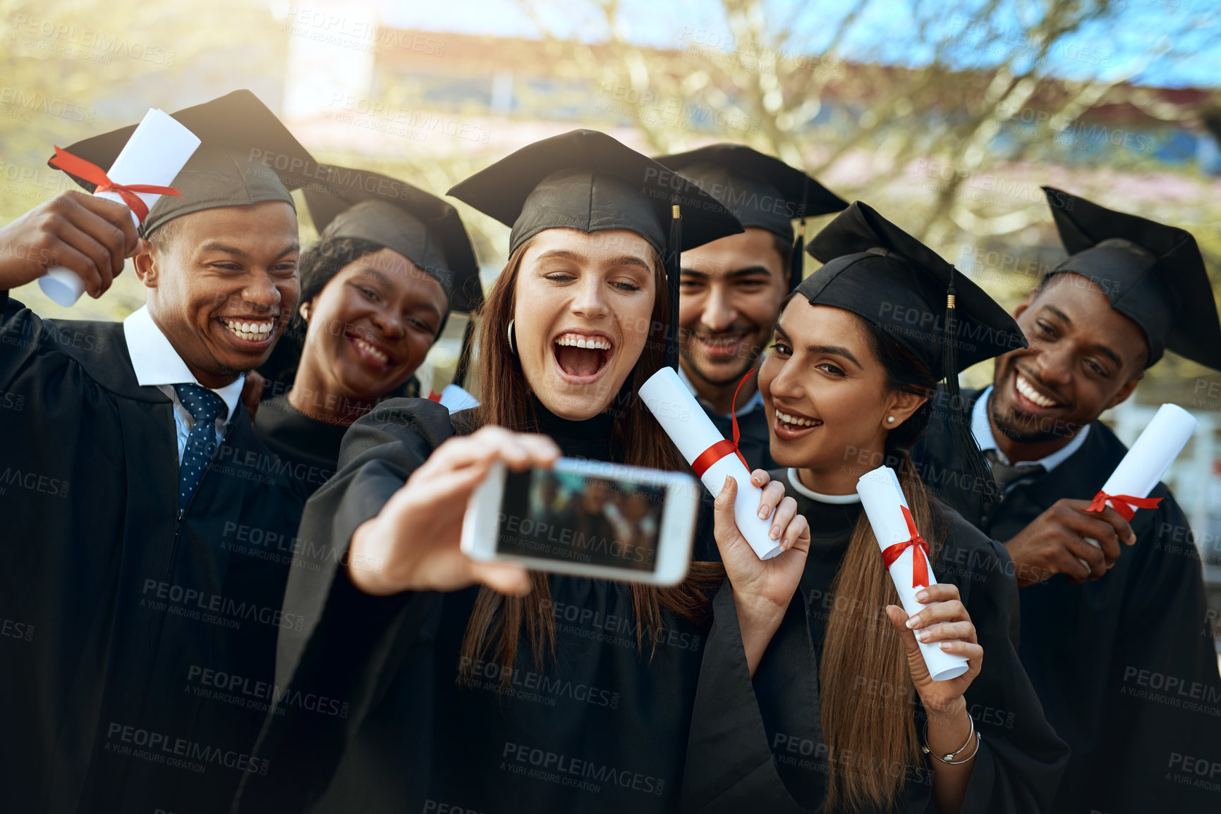 Buy stock photo Shot of a group of students taking selfies with a mobile phone on graduation day