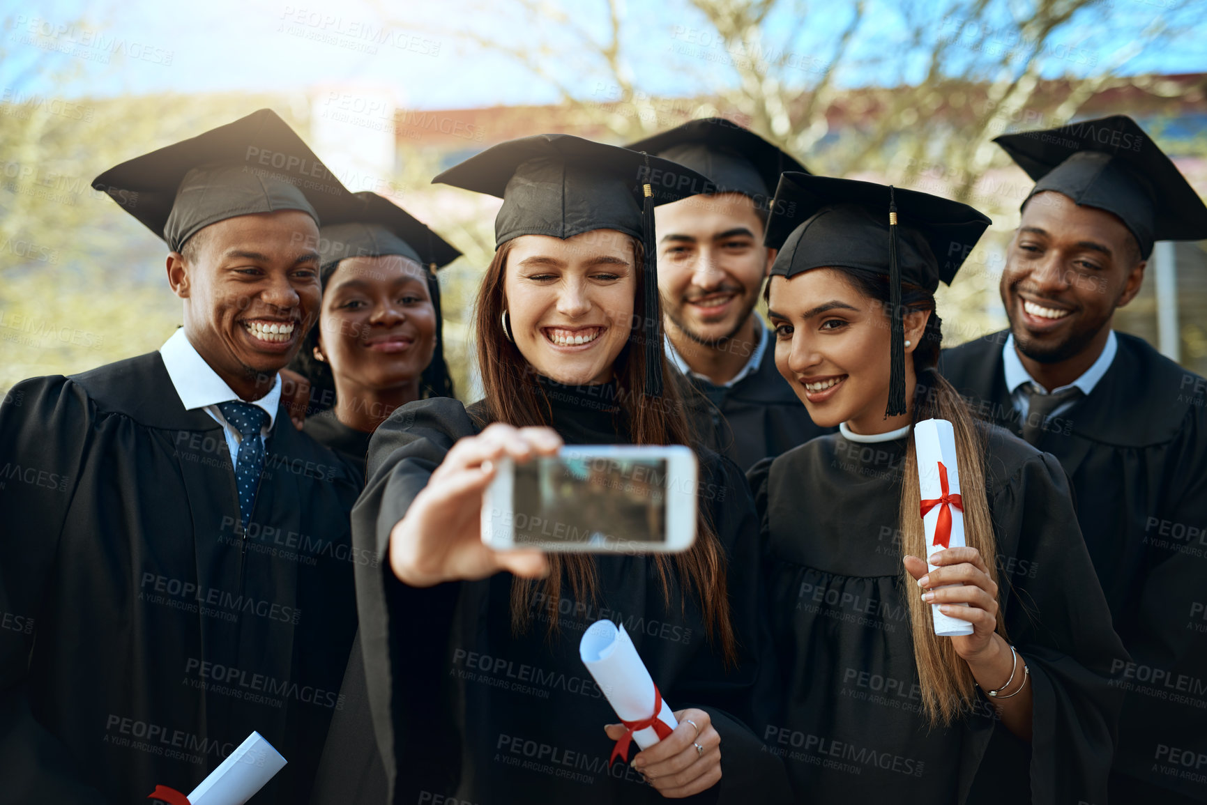 Buy stock photo Shot of a group of students taking selfies with a mobile phone on graduation day