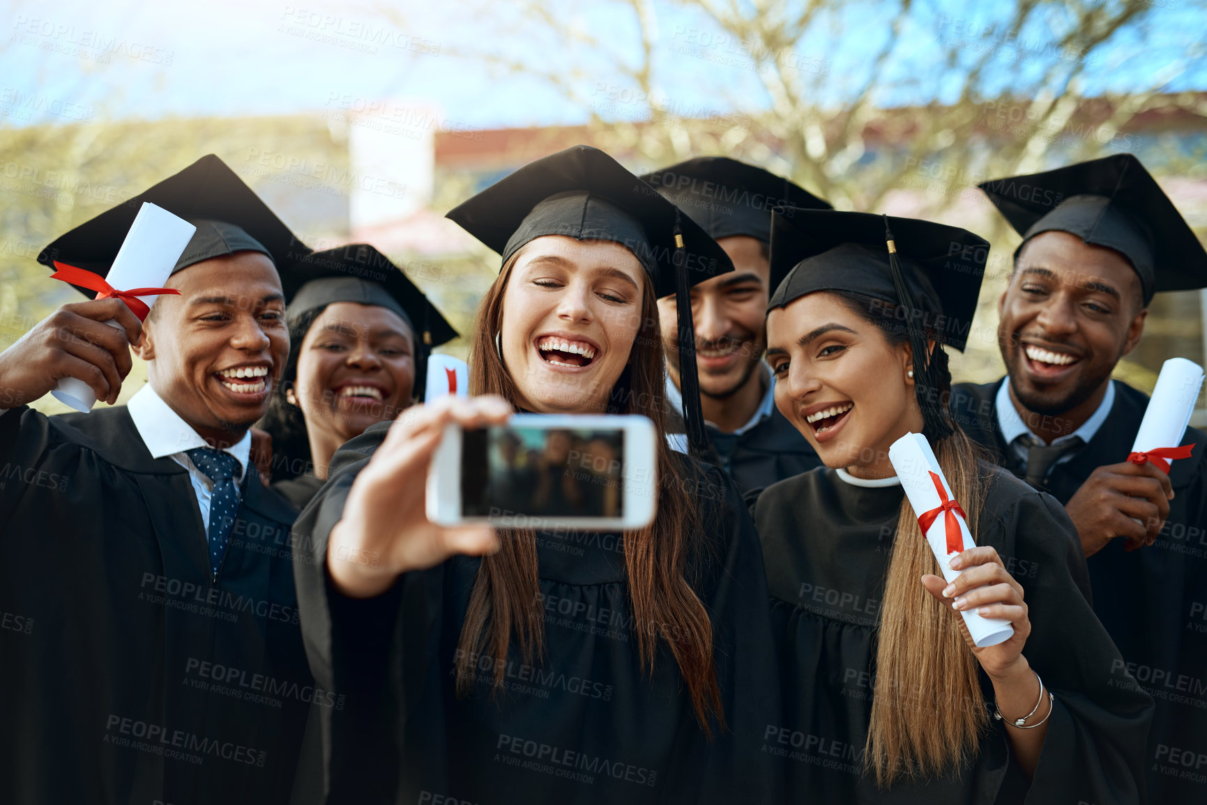 Buy stock photo Shot of a group of students taking selfies with a mobile phone on graduation day