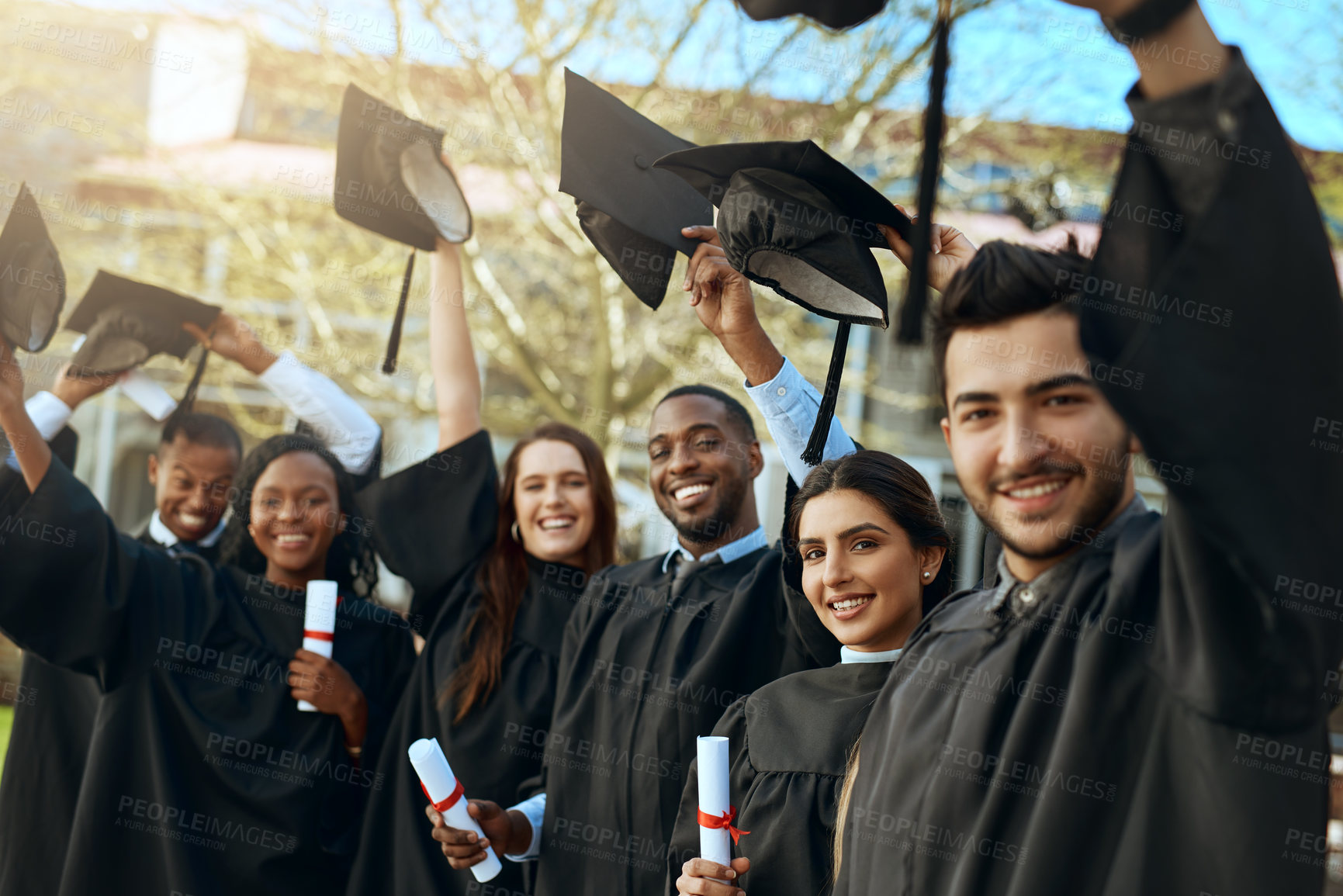 Buy stock photo Portrait of a group of happy young students taking their hats off on graduation day