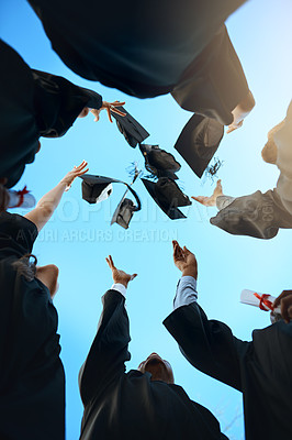 Buy stock photo Low angle shot of a group of young students throwing their hats in the air on graduation day
