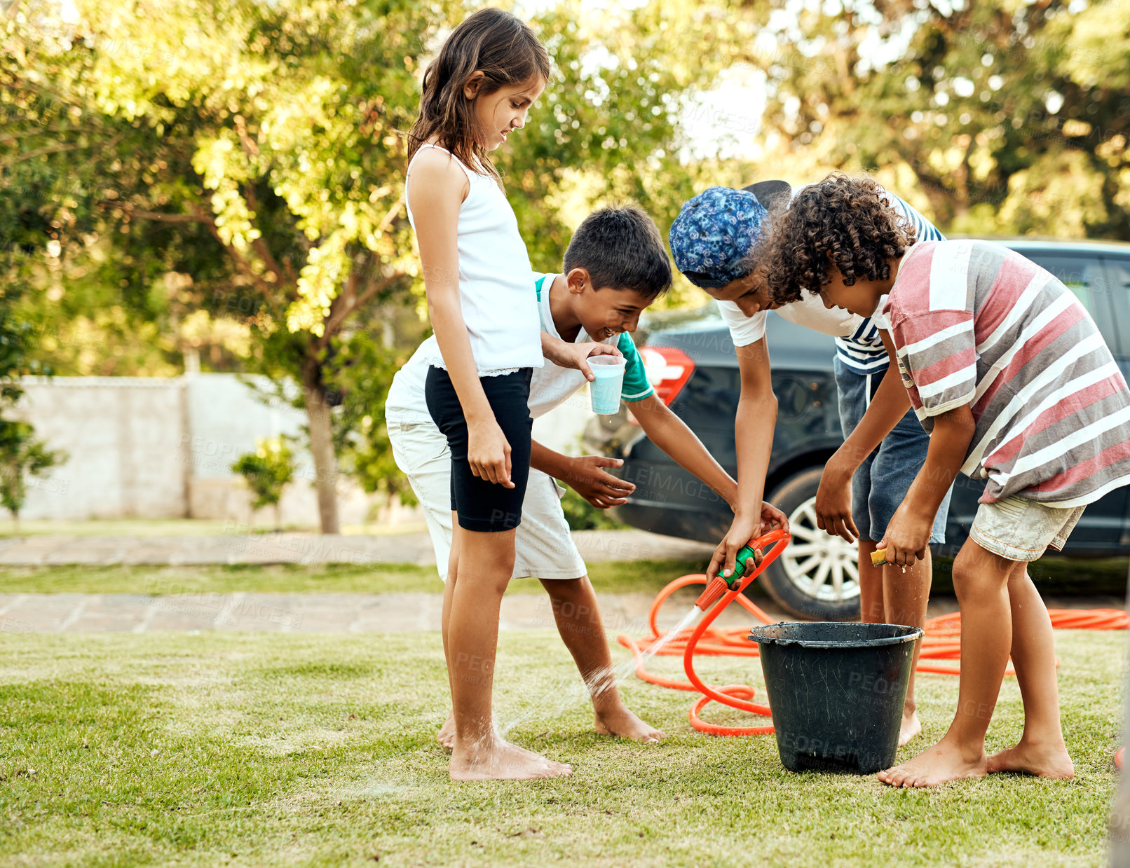 Buy stock photo Shot of a group of cheerful young kids washing their parent's car together outside during the day