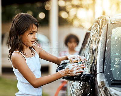 Buy stock photo Shot of a cheerful little girl washing her parent's car outside during the day