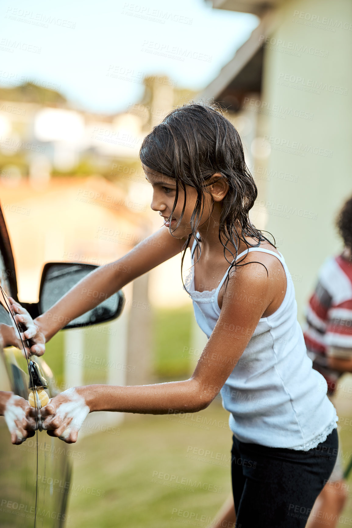 Buy stock photo Shot of a cheerful little girl washing her parent's car outside during the day