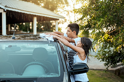 Buy stock photo Shot of two cheerful children washing their parent's car together outside during the day