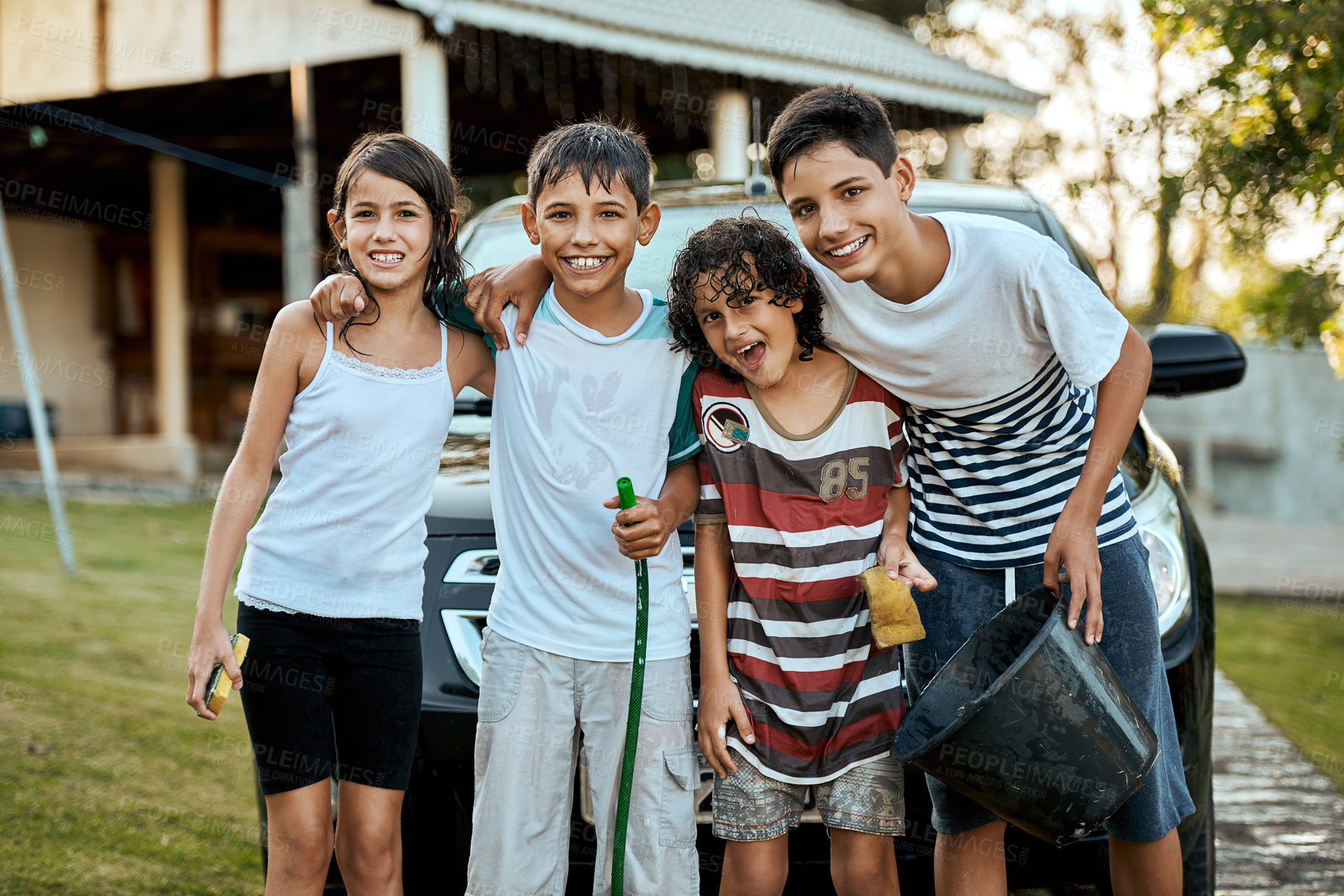 Buy stock photo Portrait of a group of young kids standing together and about to wash their parent's car outside during the day