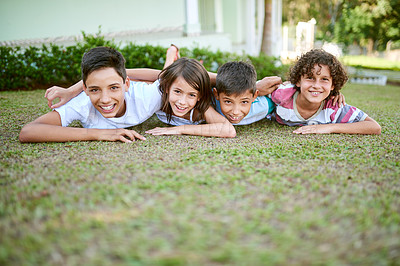 Buy stock photo Portrait of a group of happy siblings lying together on the grass in their backyard