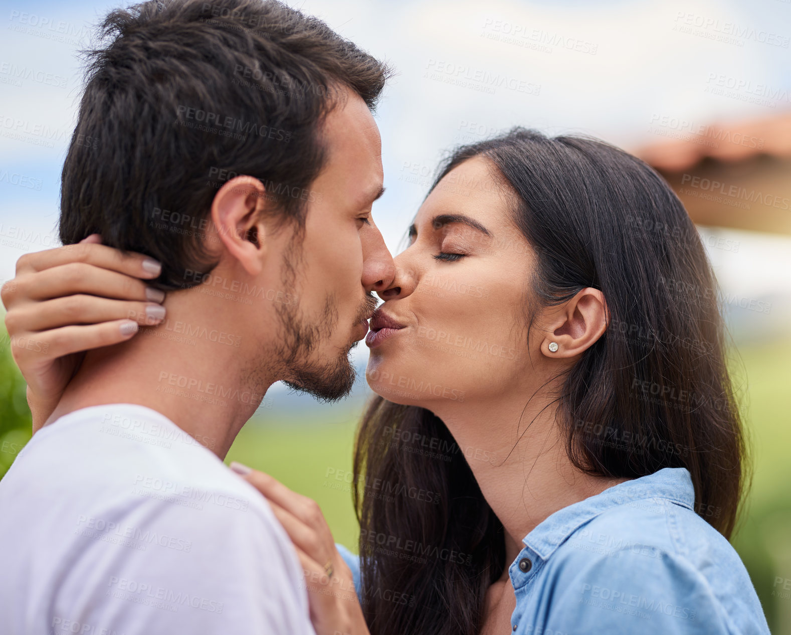 Buy stock photo Cropped shot of an affectionate young couple kissing while standing outdoors