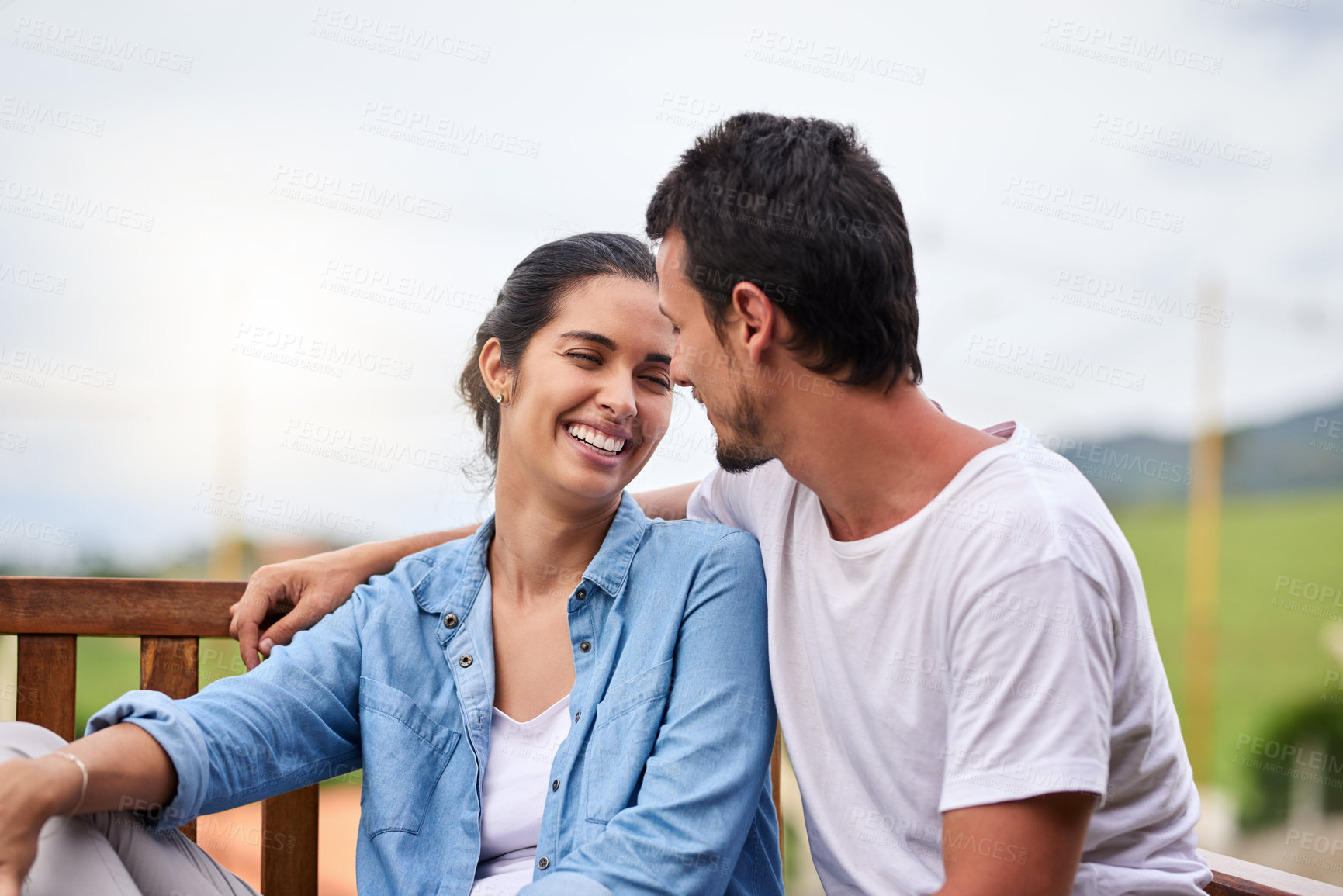 Buy stock photo Cropped shot of an affectionate young couple sitting on a bench outdoors