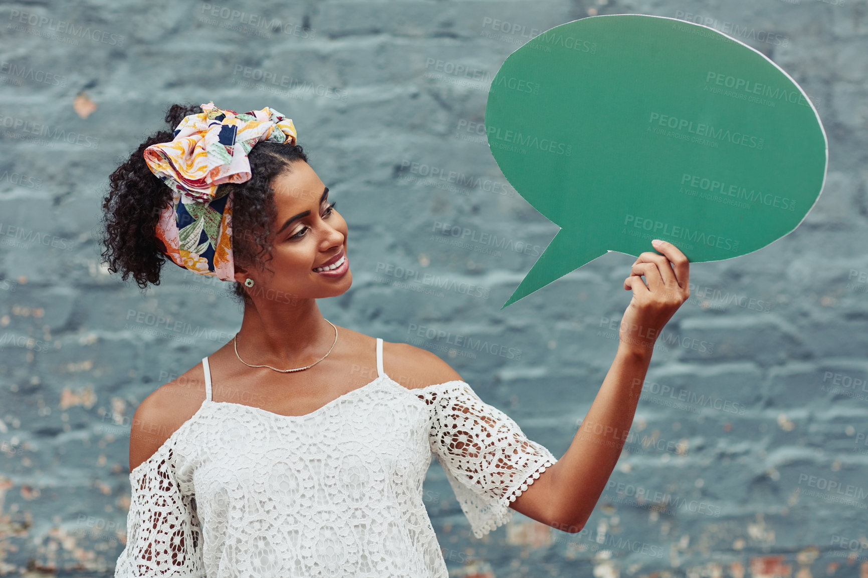 Buy stock photo Cropped shot of an attractive young woman holding a speech bubble against a brick wall outside