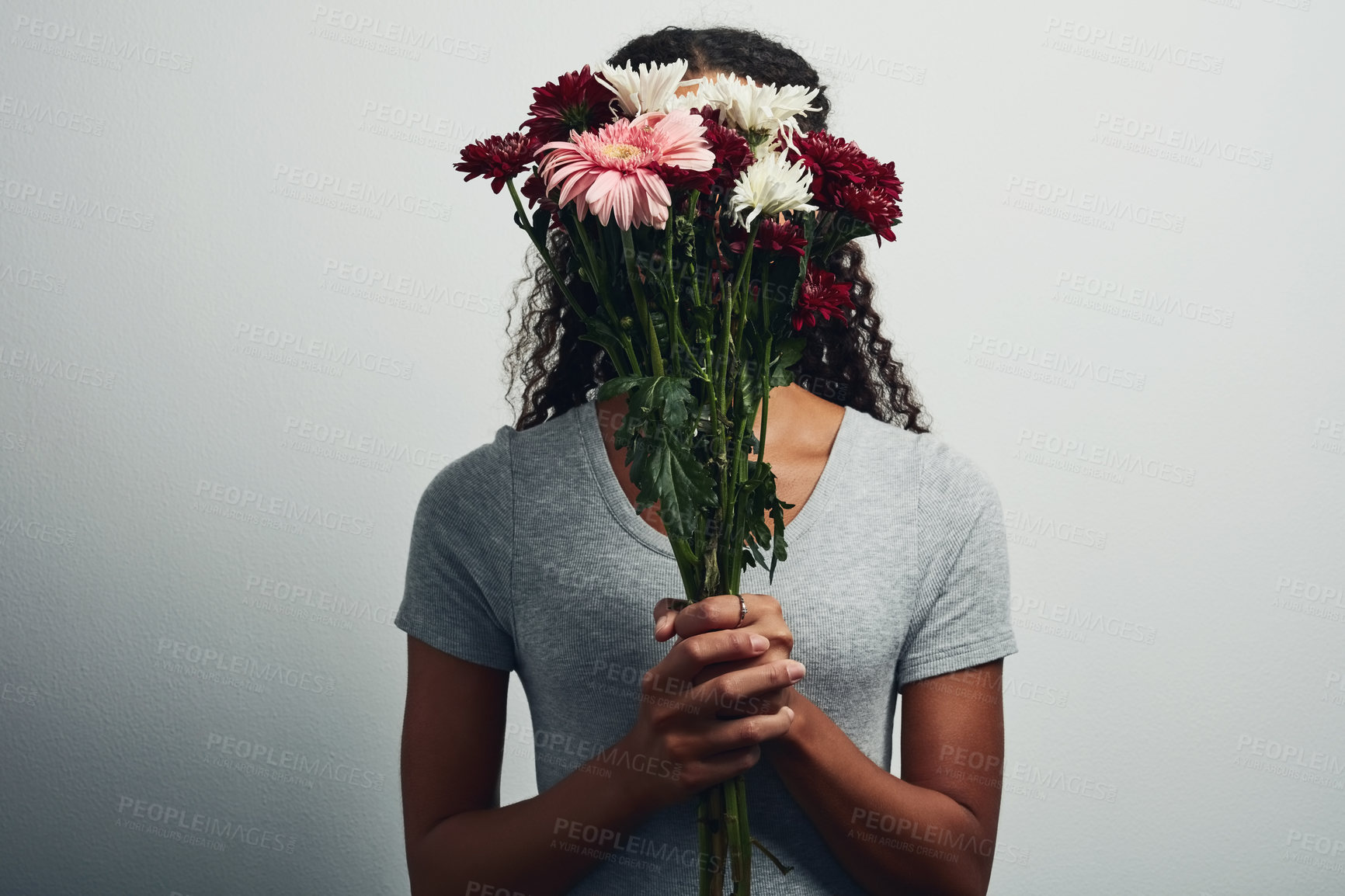 Buy stock photo Studio shot of an unrecognizable woman covering her face with a bunch of flowers against a grey background