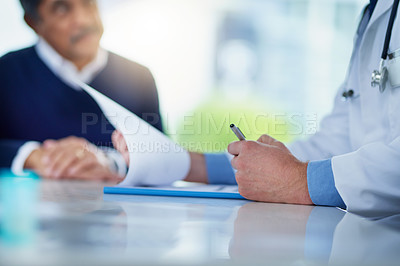 Buy stock photo Closeup shot of an unrecognizable doctor going through paperwork while having a consultation with a patient in his office