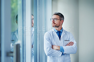 Buy stock photo Shot of a mature doctor looking out the window in a hospital