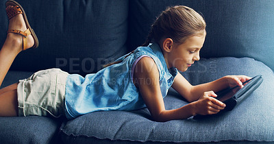 Buy stock photo Shot of a cute little girl using a digital tablet on the sofa at home