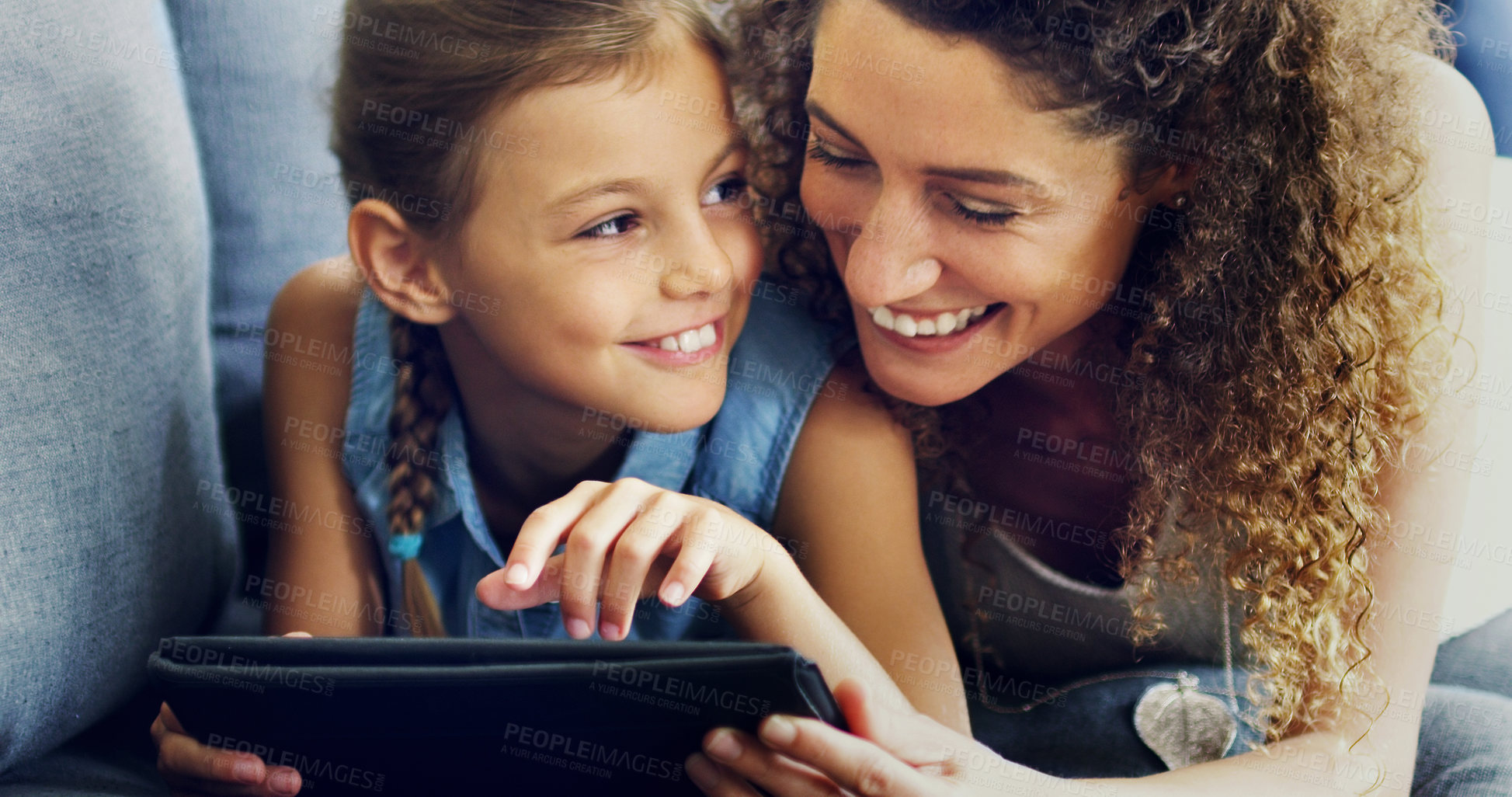 Buy stock photo Shot of a cute little girl using a digital tablet with her mother on the sofa at home