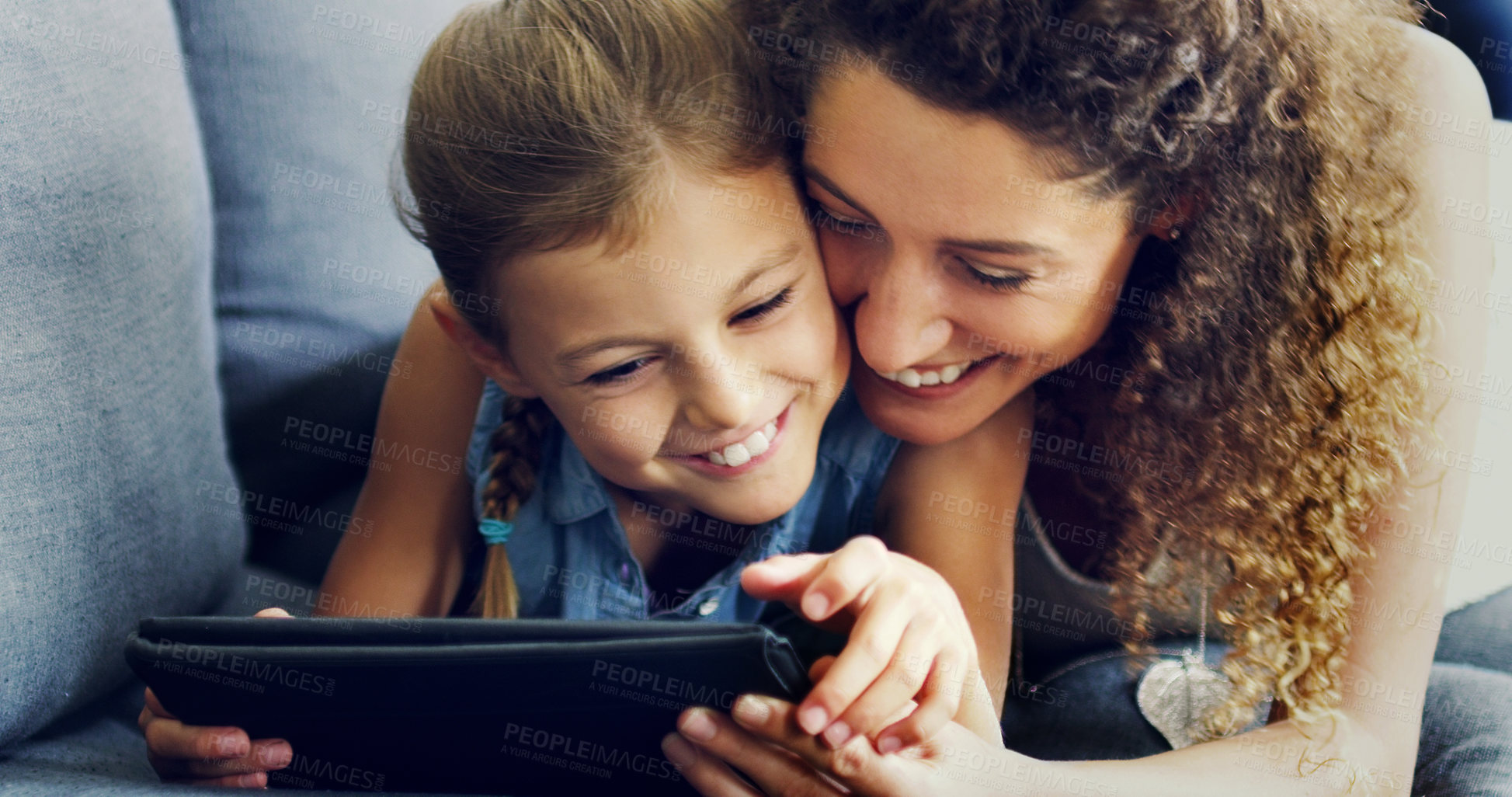 Buy stock photo Shot of a cute little girl using a digital tablet with her mother on the sofa at home