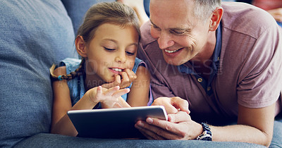 Buy stock photo Shot of a cute little girl using a digital tablet with her father on the sofa at home