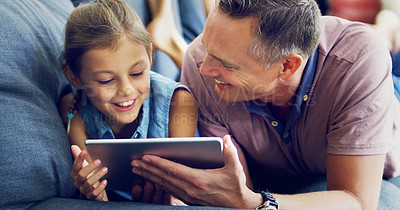 Buy stock photo Shot of a cute little girl using a digital tablet with her father on the sofa at home