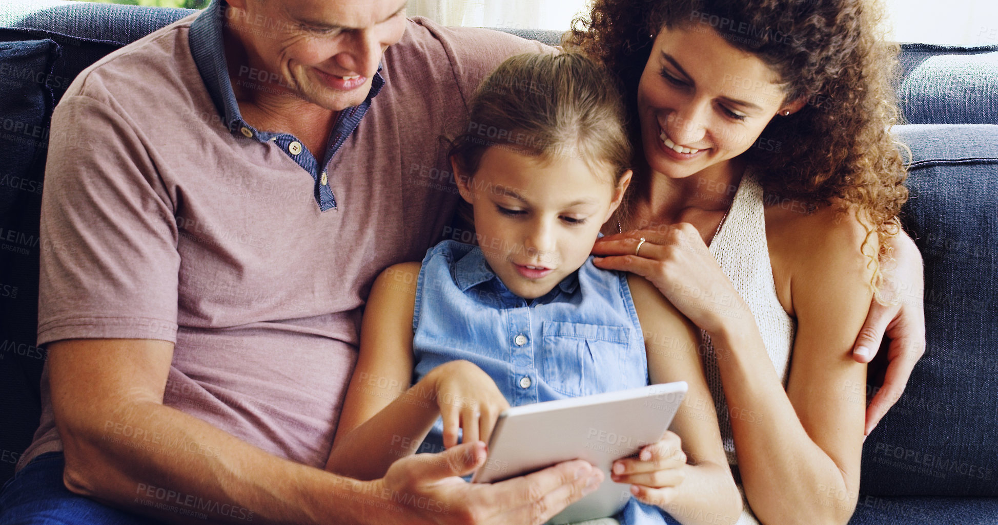 Buy stock photo Shot of a cute little girl using a digital tablet with her mother and father on the sofa at home